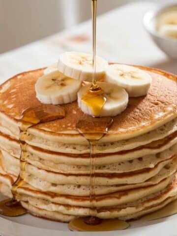 Fluffy Banana Oat Pancakes stacked high, topped with fresh banana slices, and drizzled with rich maple syrup for a wholesome and delightful breakfast treat.