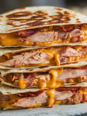 Close-up of a stacked Chicken Bacon Ranch Quesadilla with juicy chicken, crispy bacon, melted cheddar cheese, and ranch dressing, perfectly grilled for a golden, crispy texture and gooey interior.