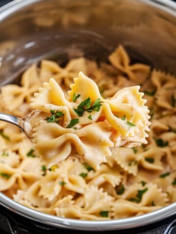 Close-up of creamy bowtie pasta topped with fresh parsley, served from an Instant Pot as part of an Instant Pot Chicken Alfredo Recipe. The pasta is rich, creamy, and perfect for a quick and delicious meal.