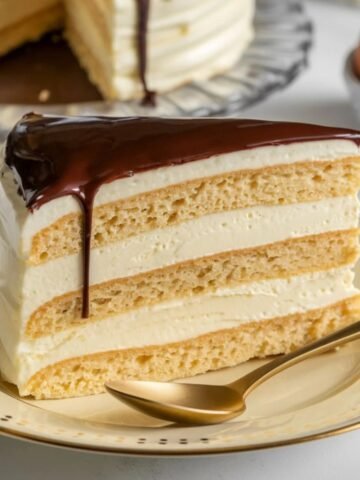 Slice of decadent Boston Cream Pie featuring layers of soft sponge cake, creamy custard filling, and a rich chocolate glaze, served on a plate with a golden spoon. Perfect dessert for any occasion.