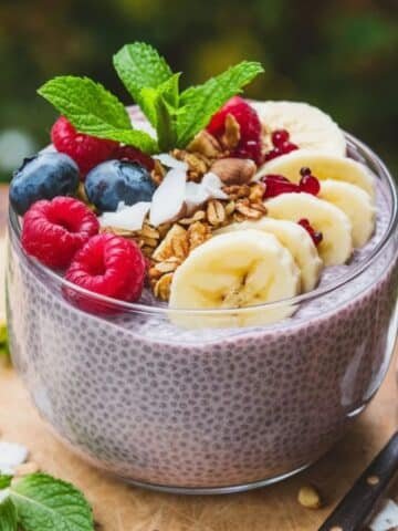 A bowl of creamy chia pudding topped with fresh raspberries, blueberries, banana slices, granola, coconut flakes, and a sprig of mint, making a nutritious and delicious chia pudding recipe." A bowl of creamy chia pudding topped with fresh raspberries, blueberries, banana slices, granola, coconut flakes, and a sprig of mint, making a nutritious and delicious chia pudding recipe."