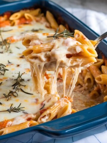 Deliciously creamy Chicken Alfredo Casserole featuring penne pasta, melted cheese, and fresh rosemary, served in a blue baking dish – an irresistible comfort food recipe.