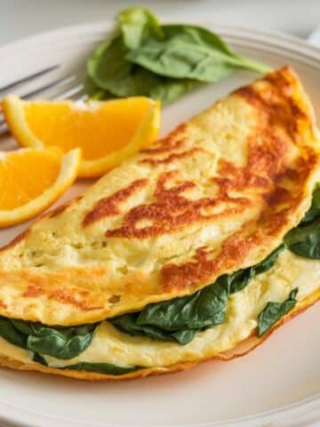 Fluffy spinach omelette paired with fresh orange wedges, offering a vibrant and nutritious breakfast option in this spinach omelette recipe.