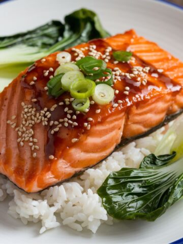 Asian salmon recipe featuring teriyaki-glazed salmon on a bed of steamed rice, garnished with sesame seeds, green onions, and served with fresh bok choy for a healthy and flavorful meal