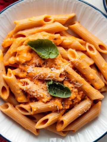 Close-up of a creamy Marry Me Pasta recipe with penne pasta, fresh basil, and grated Parmesan cheese, served on a white plate.