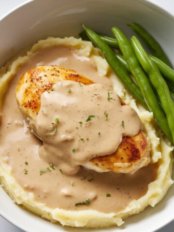 Classic Chicken and Gravy Recipe featuring a golden-brown chicken breast topped with creamy homemade gravy, served over fluffy mashed potatoes with a side of fresh green beans. A comforting and hearty meal perfect for dinner.