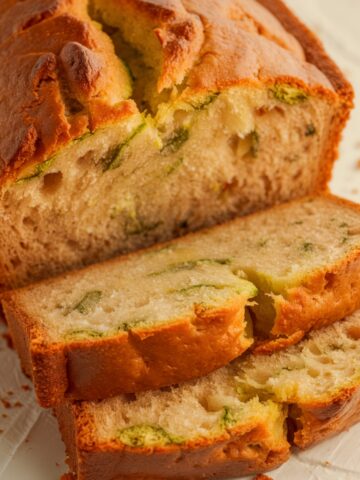 A freshly baked loaf of Gluten Free Zucchini Bread, sliced to showcase its soft, fluffy texture with tender zucchini pieces. The golden-brown crust adds a delicious contrast, making this moist and wholesome treat perfect for any occasion.