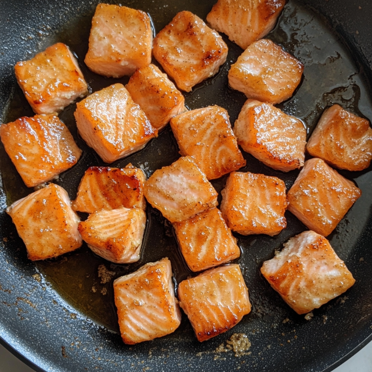 Overhead view of cooked golden salmon bites in a skillet on a white counter.