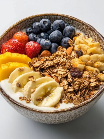 Homemade granola bowl with yogurt, fruit, and toppings on white kitchen counter