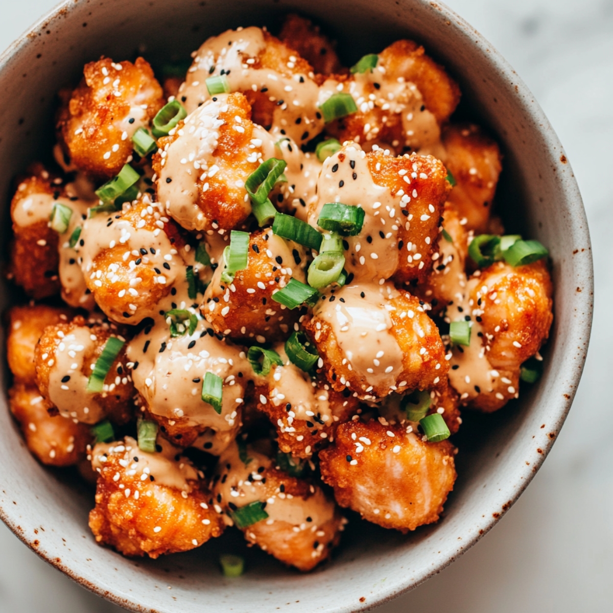 Overhead photo of crispy salmon bites coated in sauce in a mixing bowl.