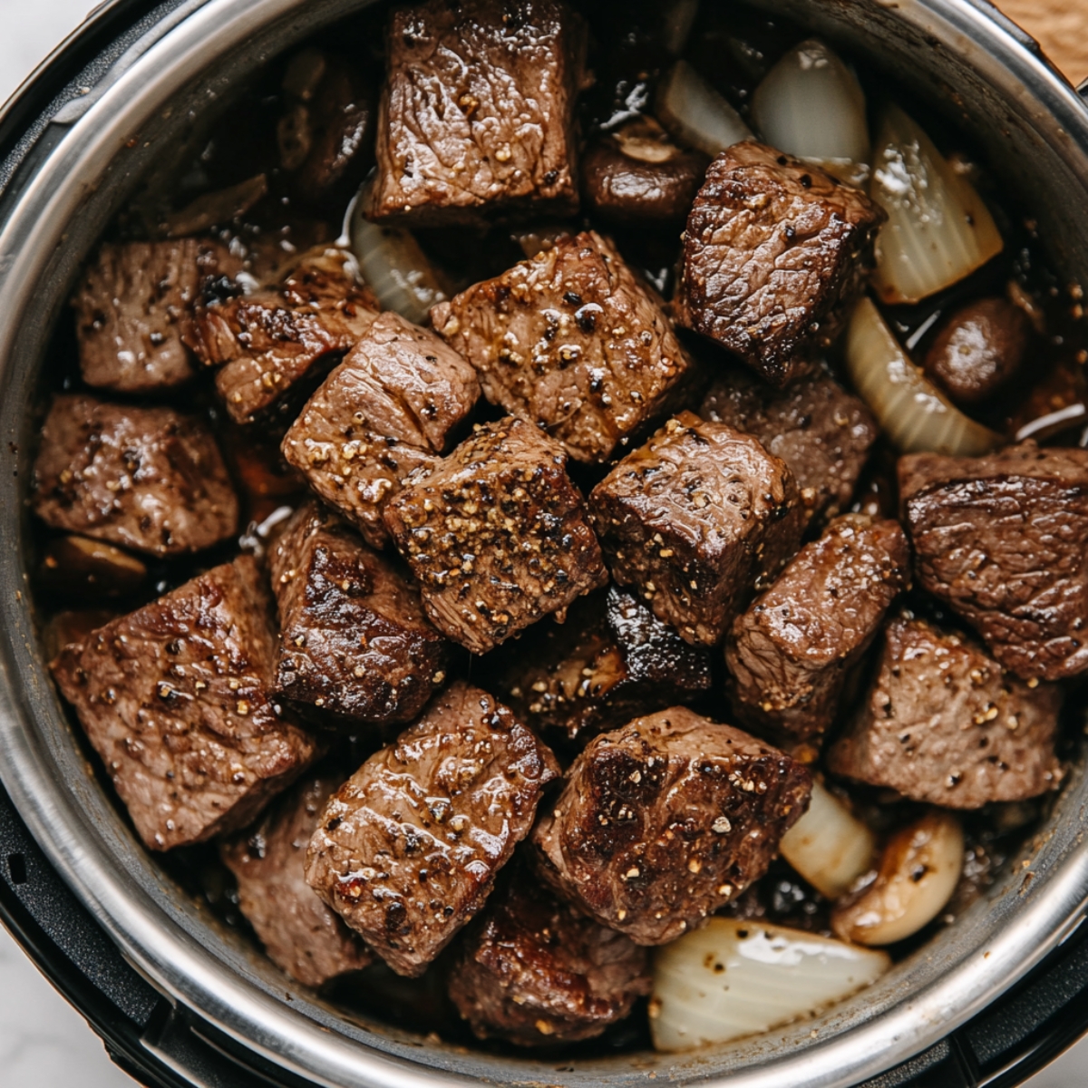 Cubed beef seared in an Instant Pot with sautéed onions and mushrooms, resting plate nearby on a white kitchen counter