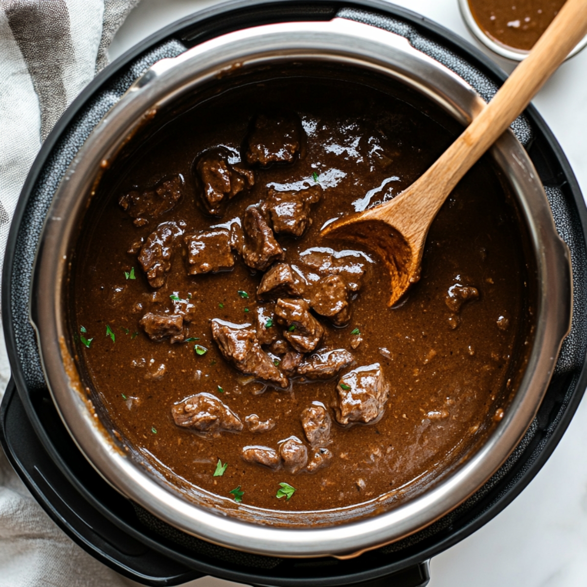 Close-up of thickened beef gravy in Instant Pot after cornstarch slurry added, with beef pieces partially visible.
