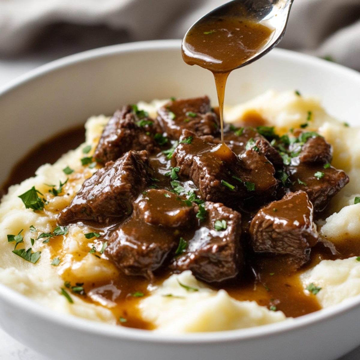Instant Pot Beef Tips served over mashed potatoes with gravy and parsley in a shallow bowl on white counter.