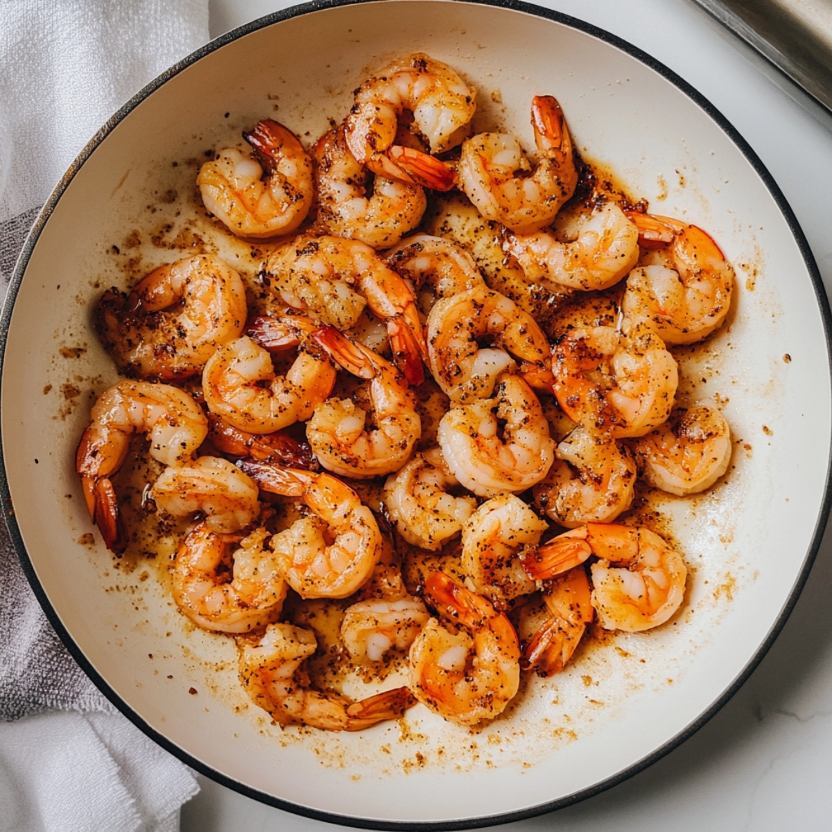 Closeup of seasoned shrimp seared to golden on a white skillet
