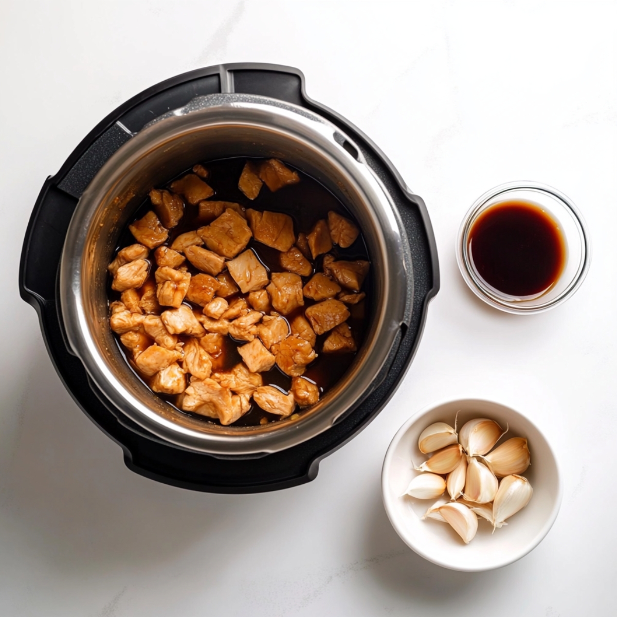 Raw chicken pieces browning in an Instant Pot next to a bowl of teriyaki sauce ingredients on a white kitchen counter.