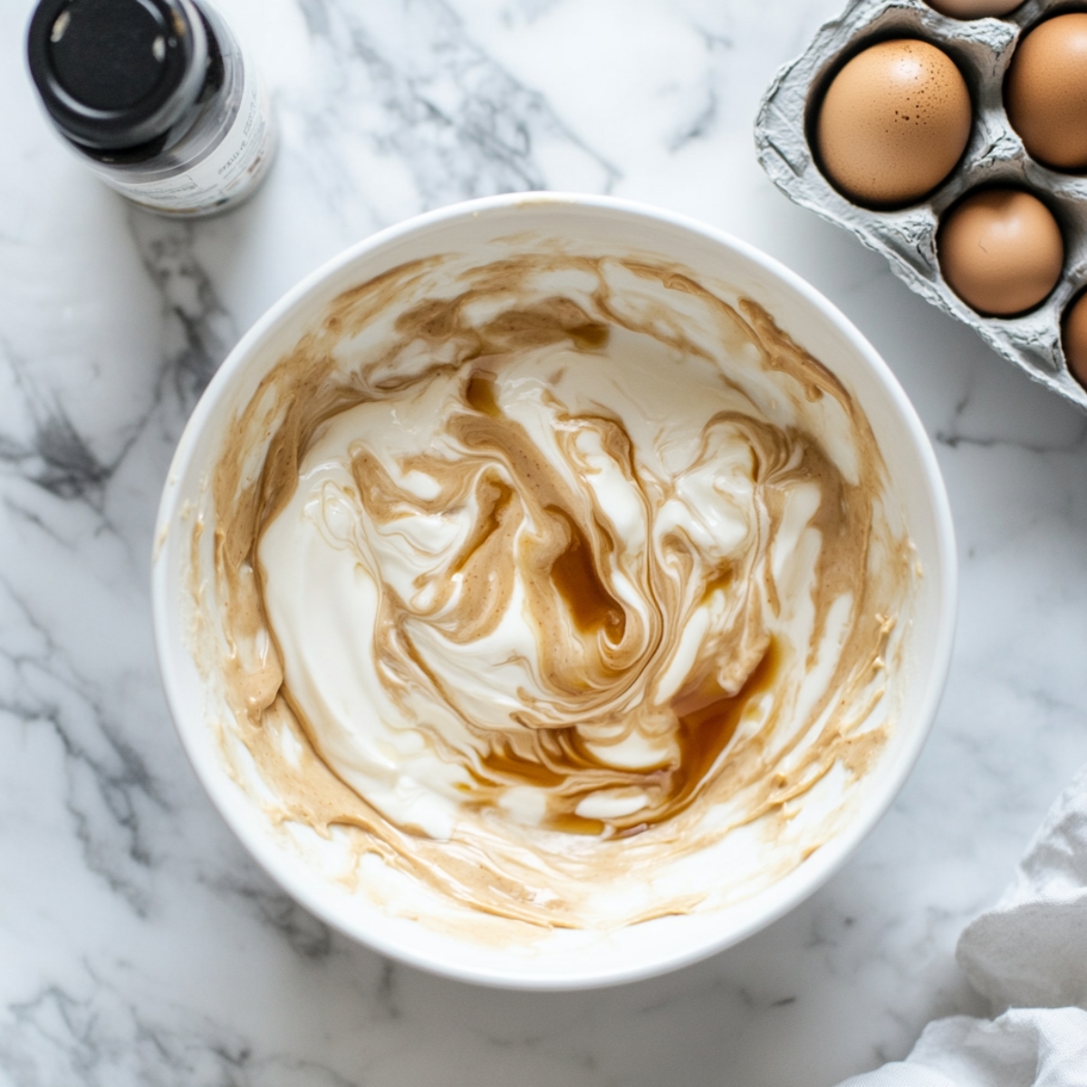 Wet mixture for protein brownies in glass bowl with nearby dry ingredients


