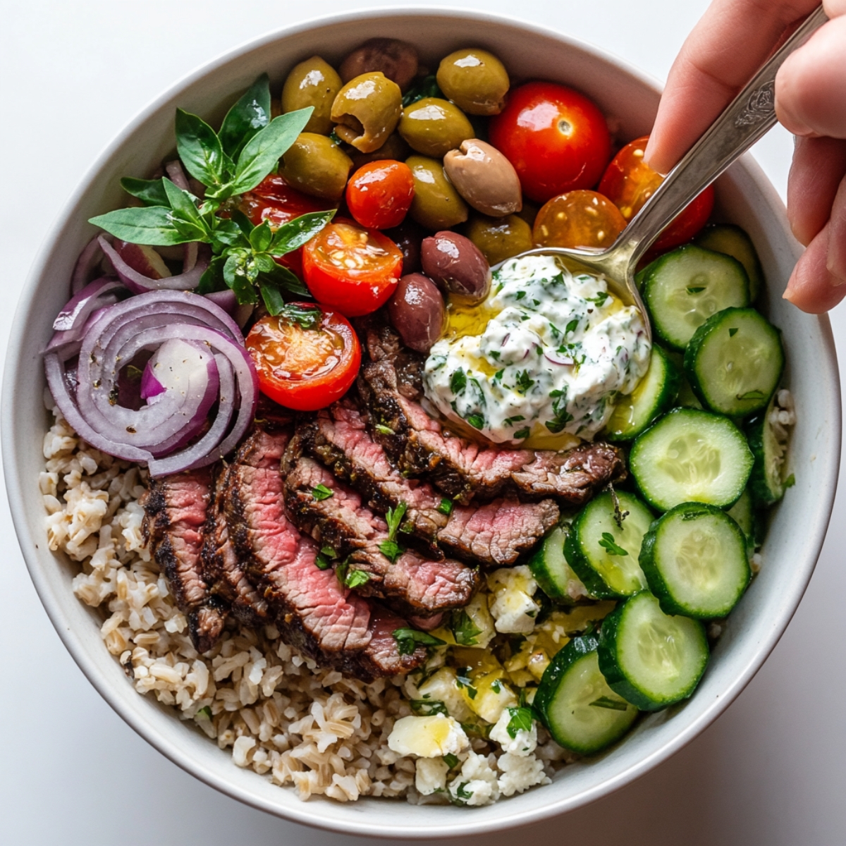 Mediterranean steak bowl being assembled with fresh toppings
