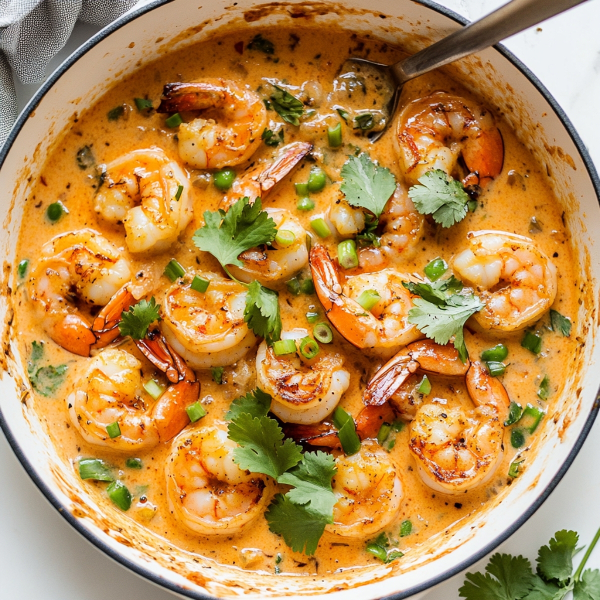 Finished creamy coconut shrimp garnished with herbs in skillet