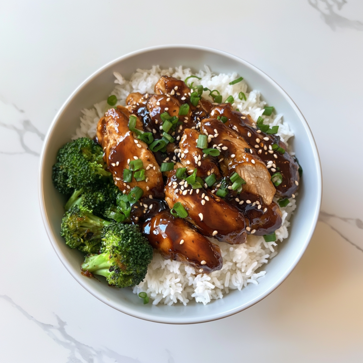  Chicken teriyaki served on rice, topped with green onions and sesame seeds, on a white kitchen counter.