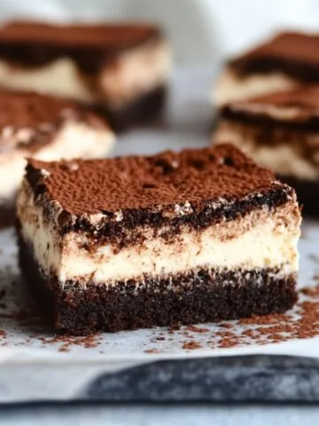 Close-up of a tiramisu brownie with creamy mascarpone layer and cocoa powder topping on parchment paper