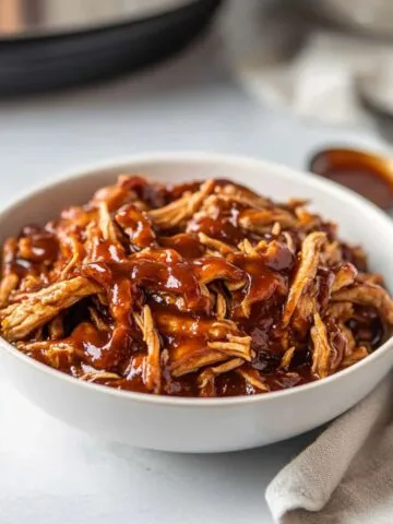 BBQ shredded chicken served in bowl with barbecue sauce on white counter