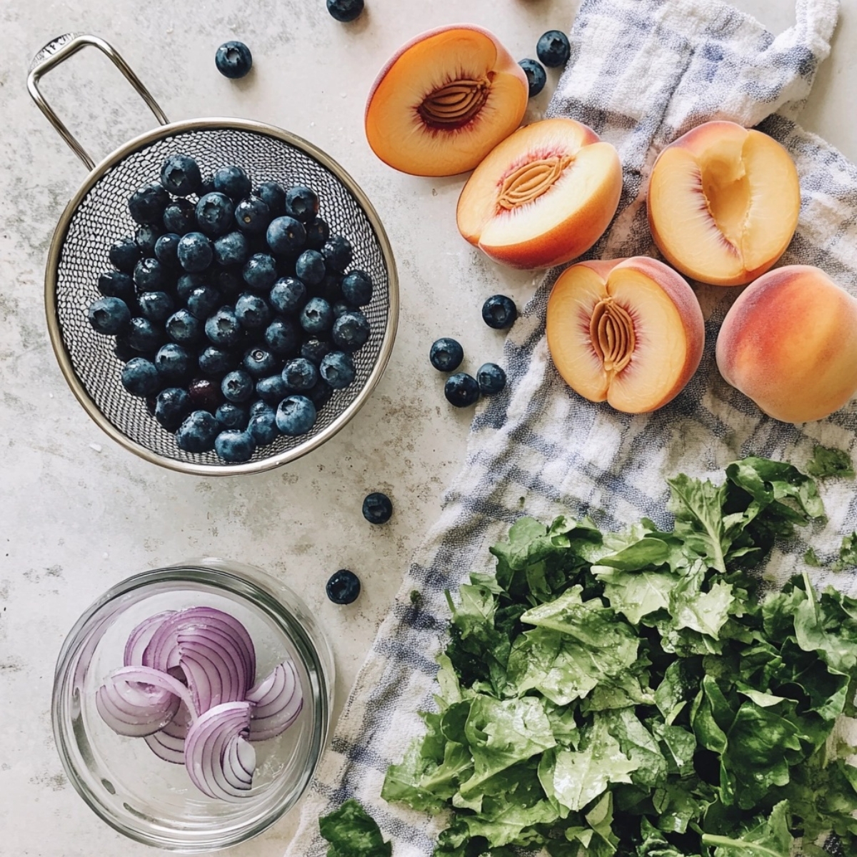 Sliced peaches, blueberries, onions, and greens on a white kitchen counter