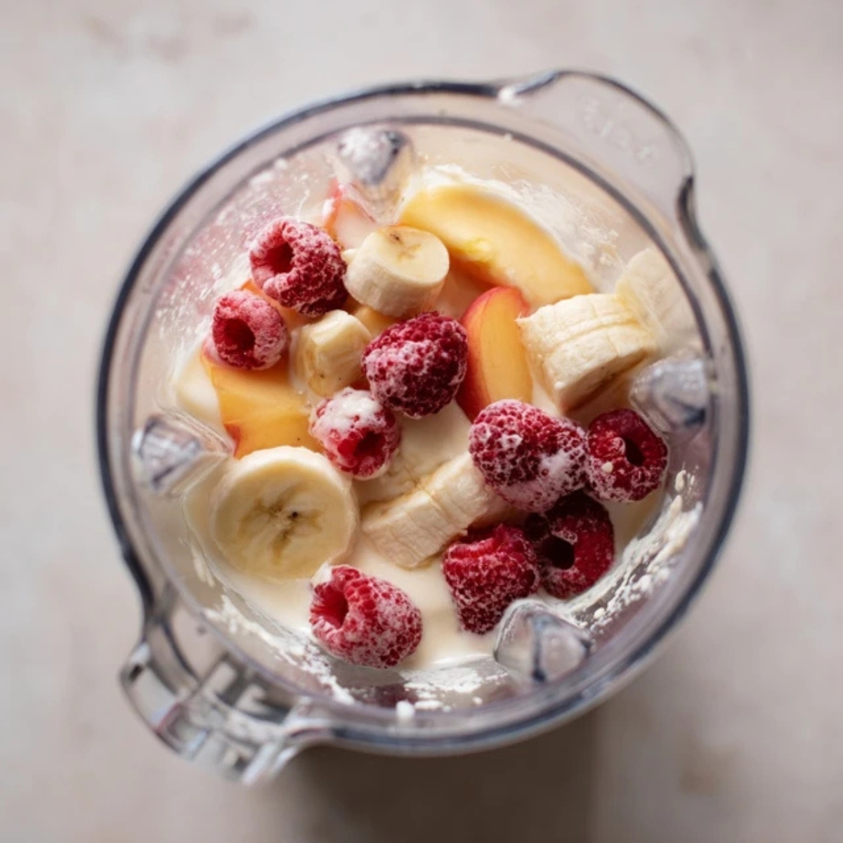 Unblended raspberry peach smoothie ingredients layered in blender

