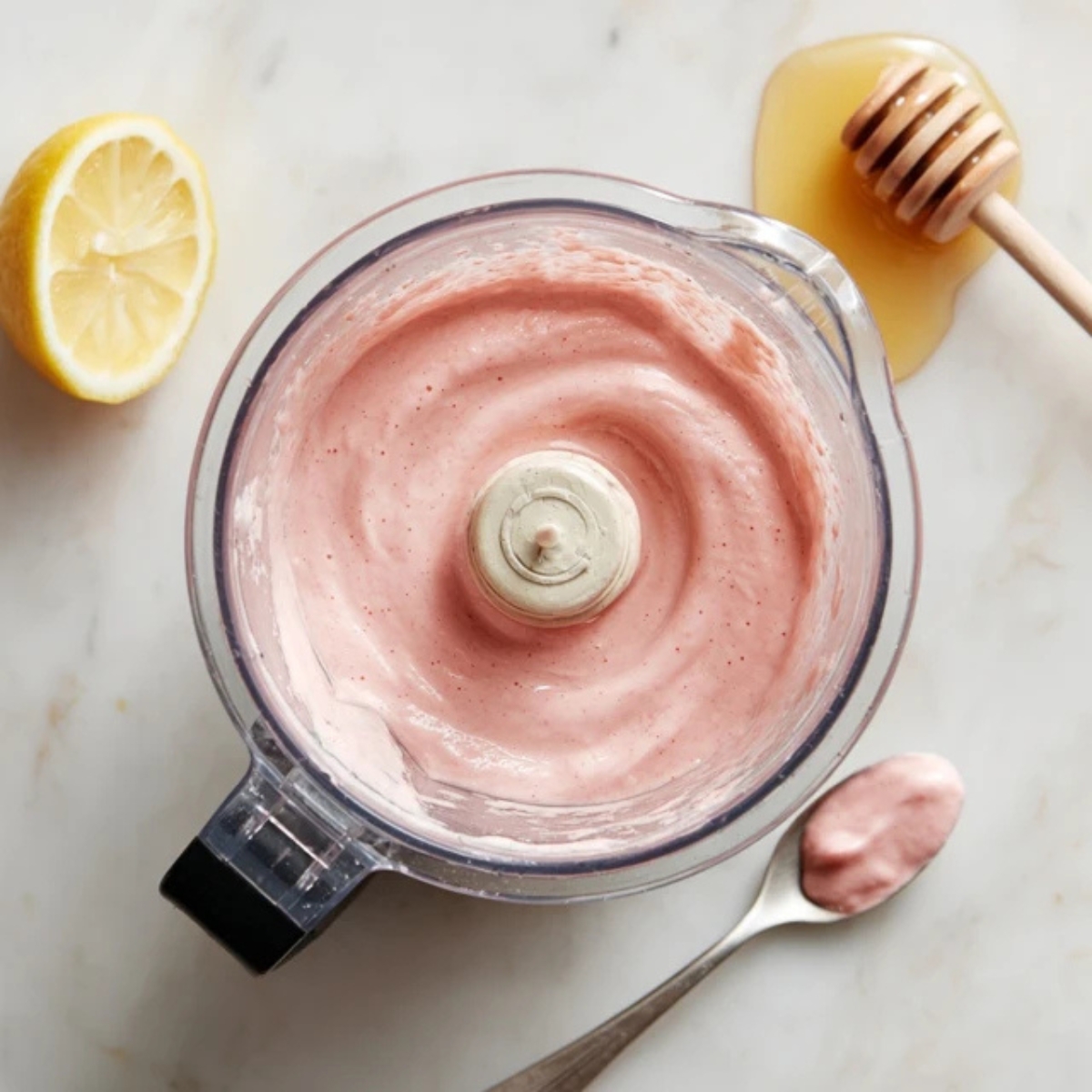 Tasting spoon next to creamy raspberry peach smoothie in blender

