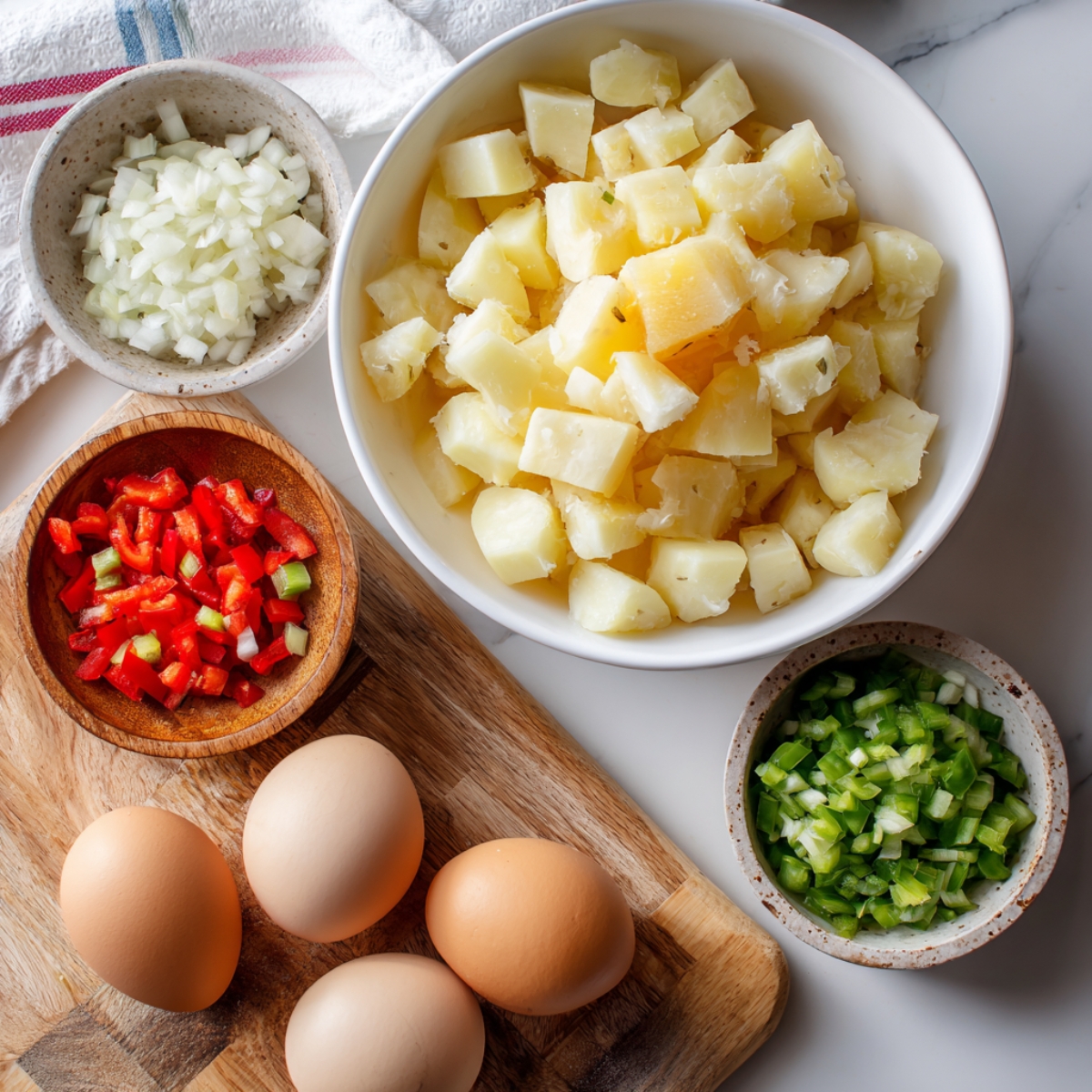 diced potatoes, cracked eggs, and chopped veggies on white counter