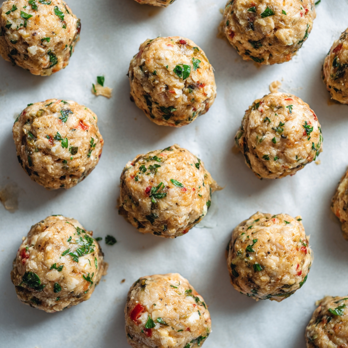 raw shaped Italian chicken meatballs on parchment-lined tray