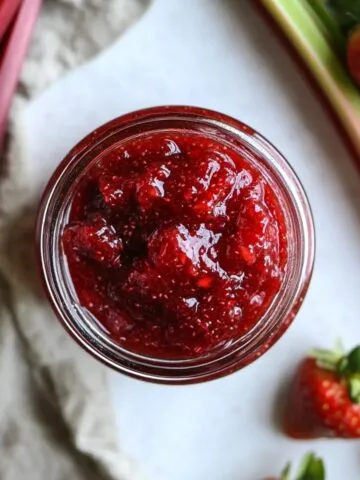 Jar of strawberry rhubarb jam recipe with toast on white counter