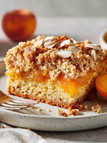 Moist apricot cake slice on a white plate with crumb topping and fresh apricots