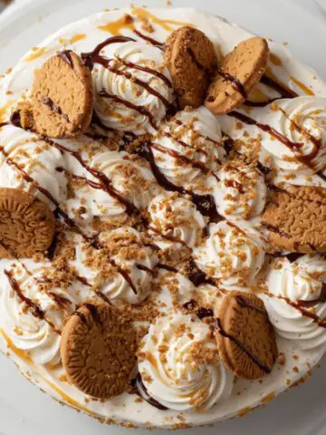 Homemade Biscoff cream cake recipe with cookie drizzle and cookie topping on a white kitchen counter