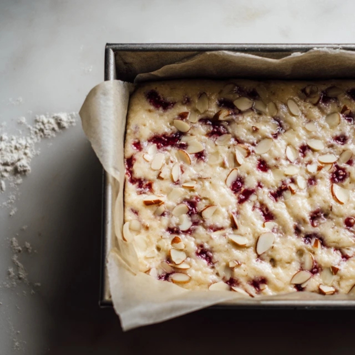 Cherry almond cake batter in silver pan on white counter