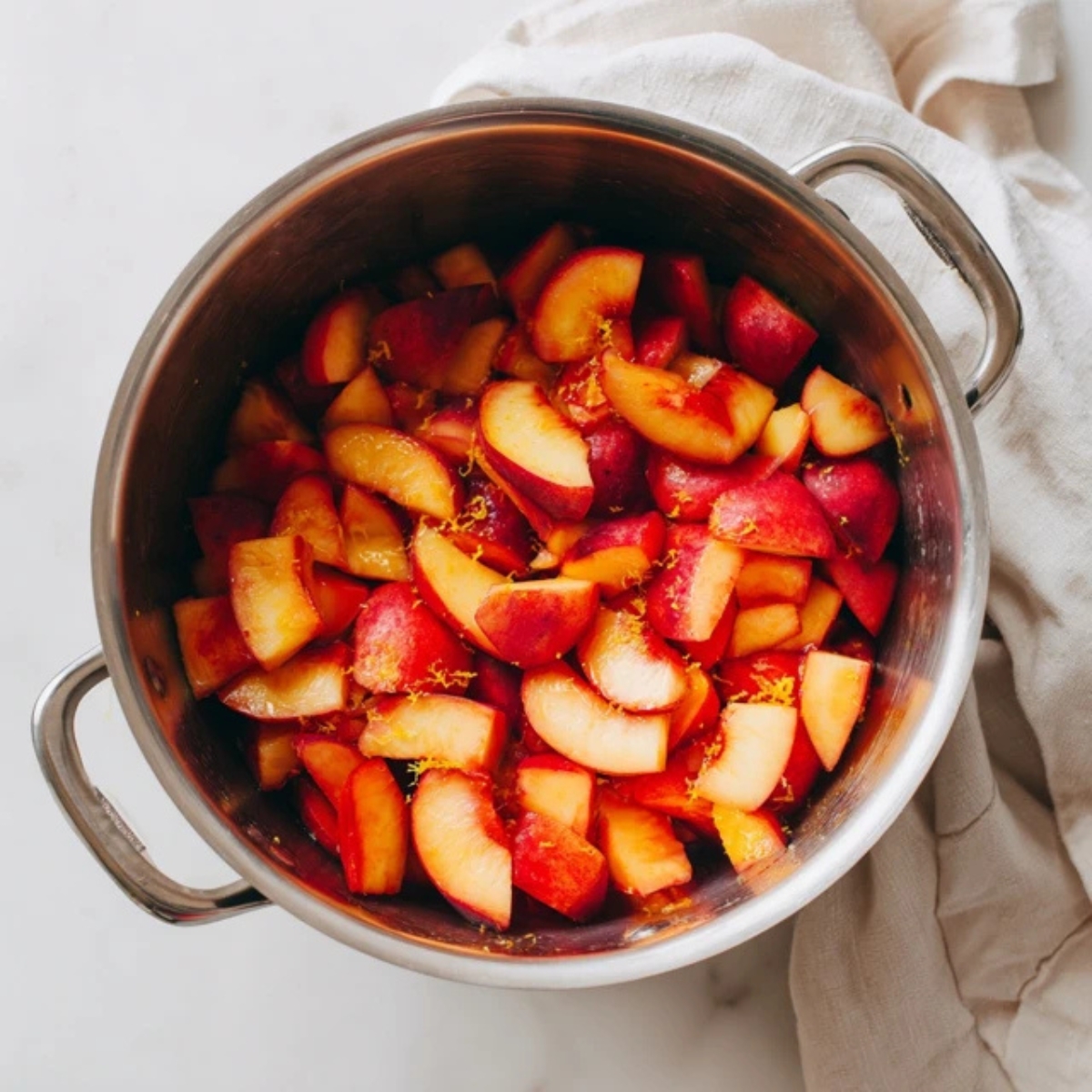 Chopped nectarines with lemon zest in a pot on white counter

