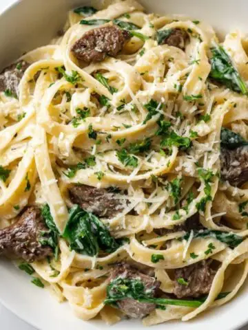 Creamy steak pasta with spinach in white bowl on kitchen counter