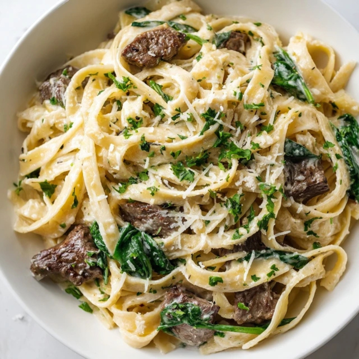 Creamy steak pasta with spinach in white bowl on kitchen counter