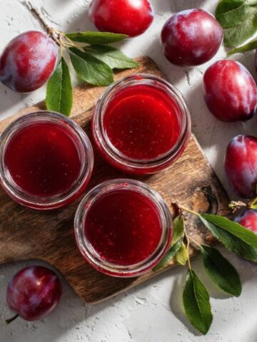 Homemade plum jelly in glass jars with fresh plums on white kitchen counter