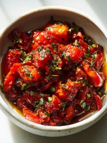 Bowl of homemade stewed tomatoes on a white counter, with visible herbs and a chunky, rustic texture.