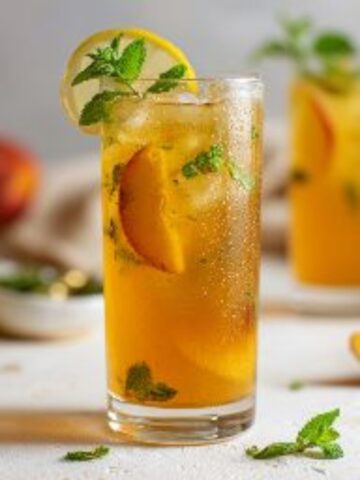 Homemade iced peach green tea lemonade in glass with lemon and mint