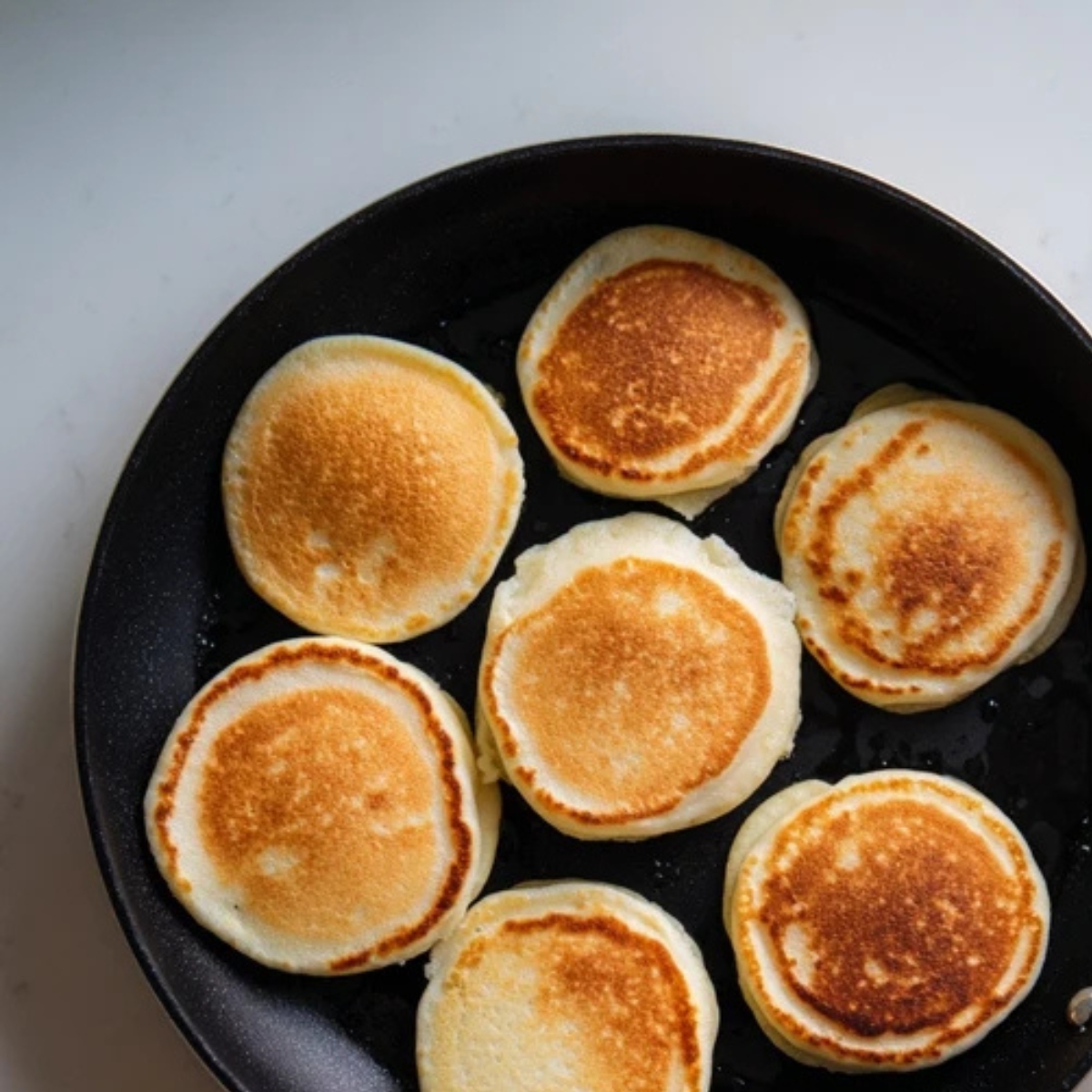 Mini pancakes bubbling on skillet with spatula beside