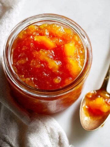 Jar of homemade nectarine jam with spoon on white counter
