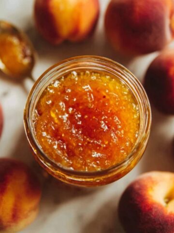 open jar of peach jam recipe with spoon and toast on white counter