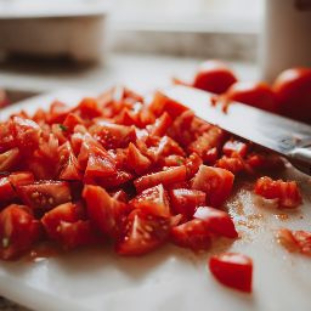 Chopped peeled tomatoes with bits of skin and juice on a white counter, ready for stewing.

