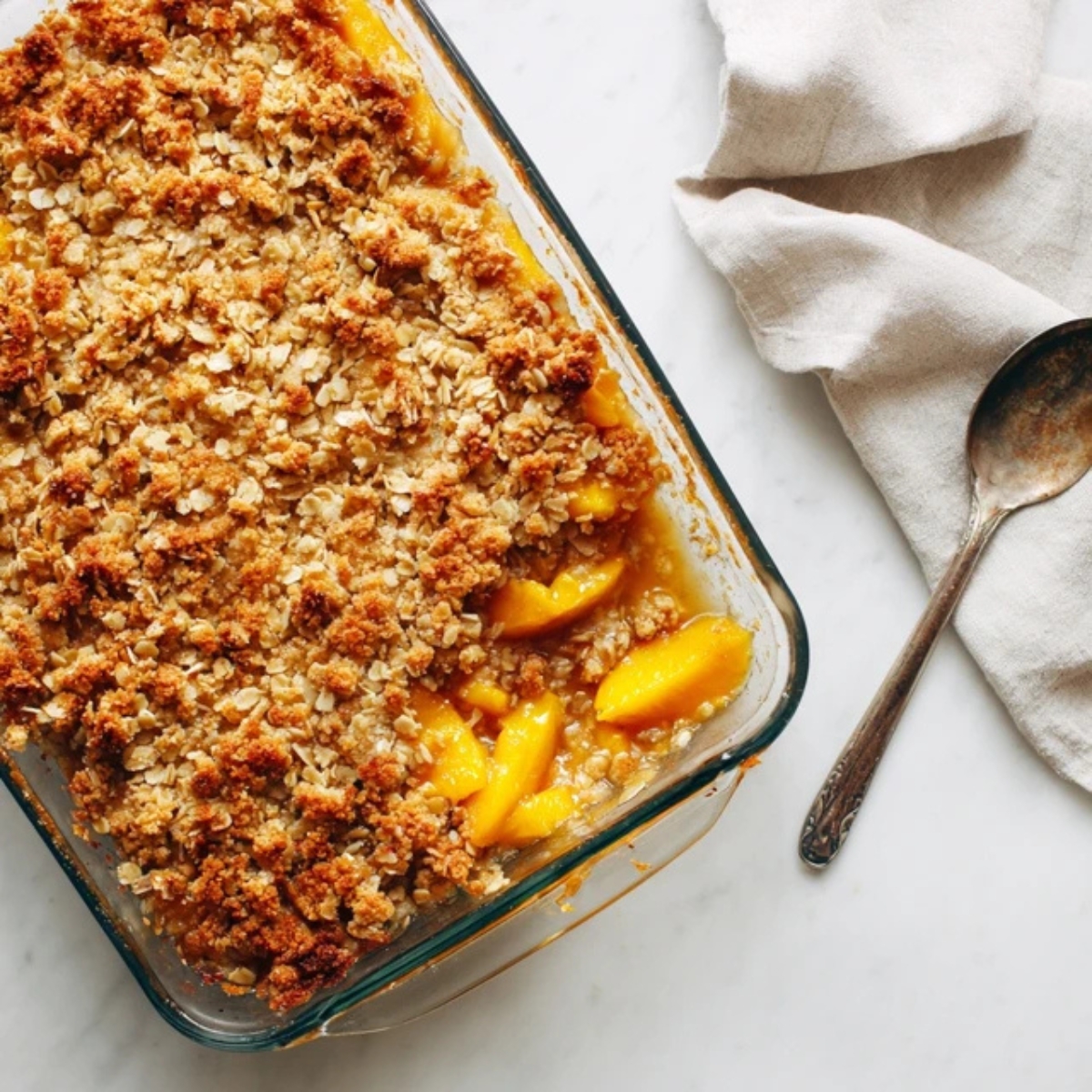 Rustic nectarine crisp with golden oat topping in glass dish

