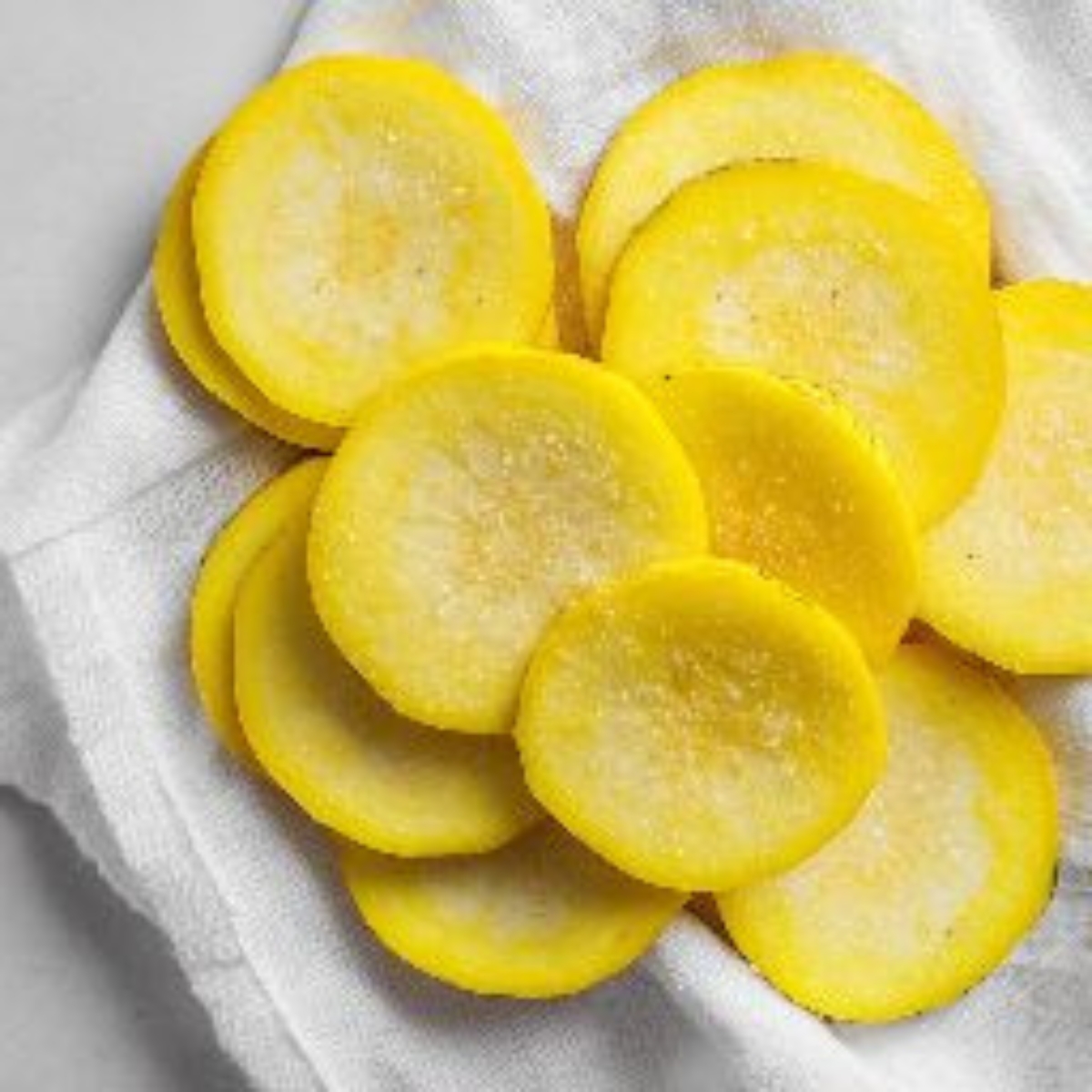 Sliced salted squash rounds resting on paper towels on a white countertop