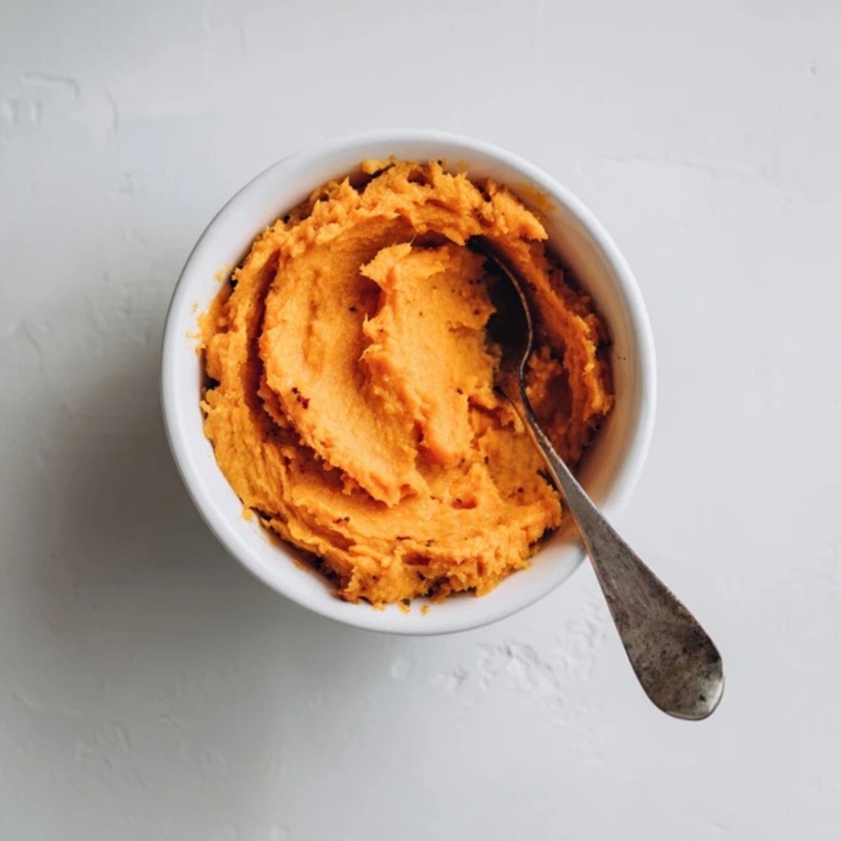 Bowl of mashed sweet potato on white kitchen counter

