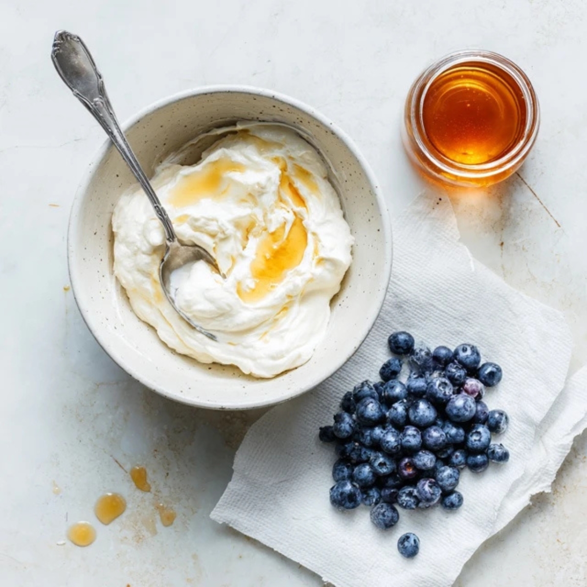 Mixing yogurt and honey for blueberry yogurt bites on a white kitchen counter