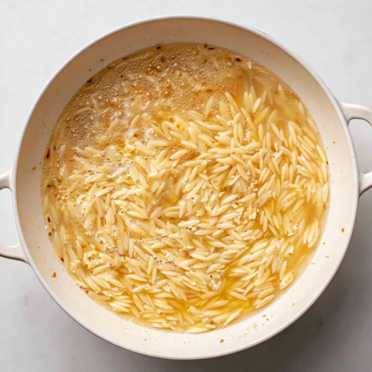 Orzo pasta simmering in broth in a white skillet