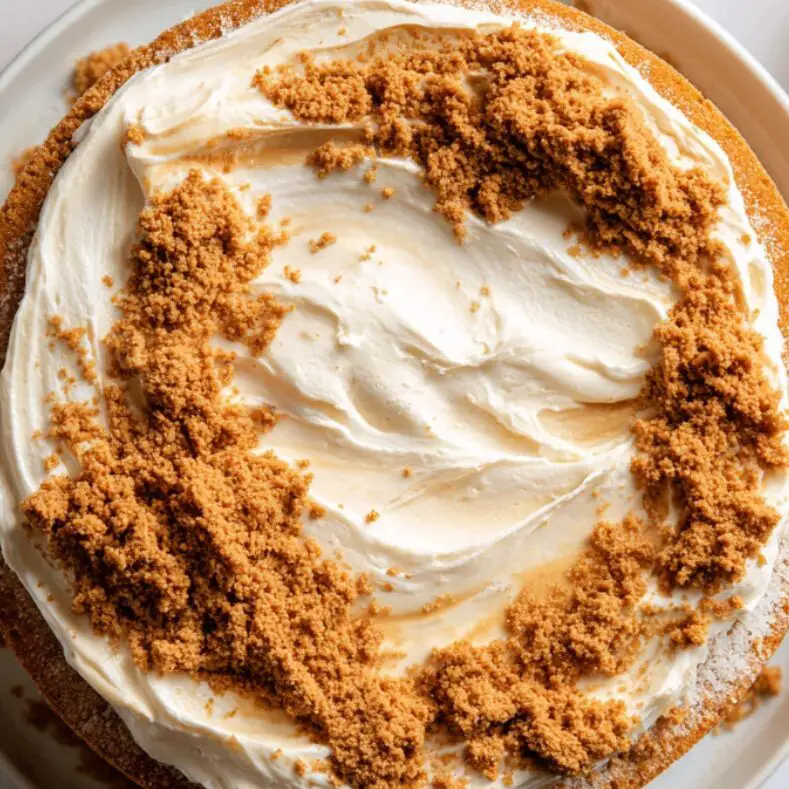 Layering Biscoff cream and crushed cookies between sponge cakes on a white counter

